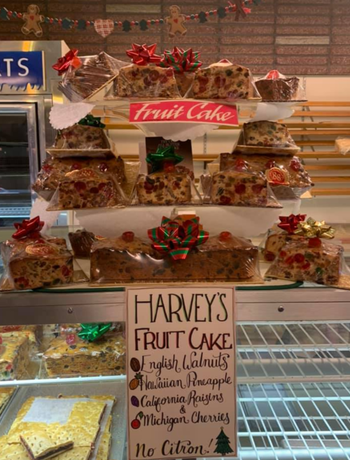 A display of fruit cakes with festive decorations, labeled "Harvey's Fruit Cake," featuring various flavors and ingredients.