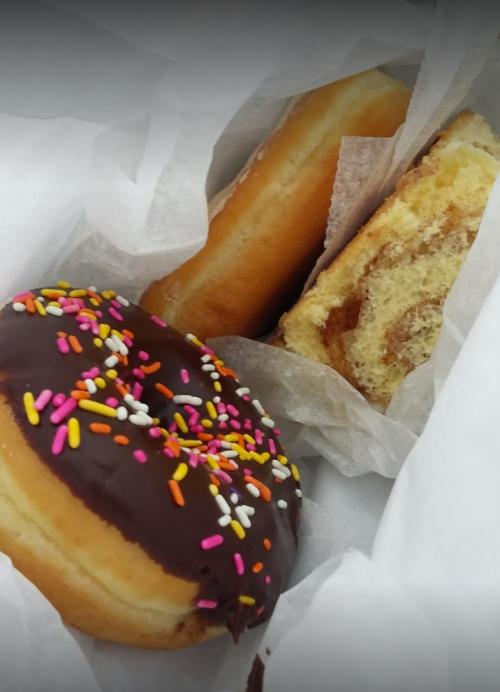 A box containing three donuts: one chocolate frosted with sprinkles, one plain, and one cinnamon swirl.