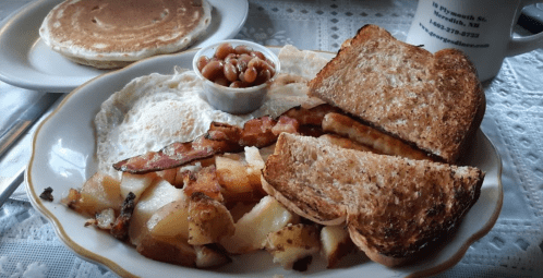 A hearty breakfast plate with eggs, bacon, toast, potatoes, baked beans, and a side of pancakes.