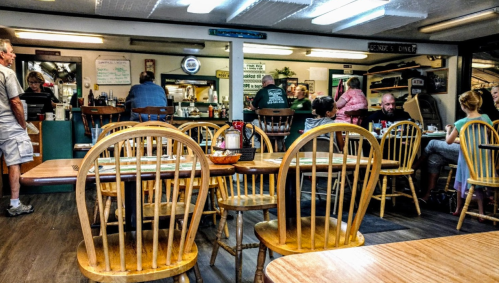 A cozy diner interior with wooden tables and chairs, patrons enjoying meals, and staff at the counter.