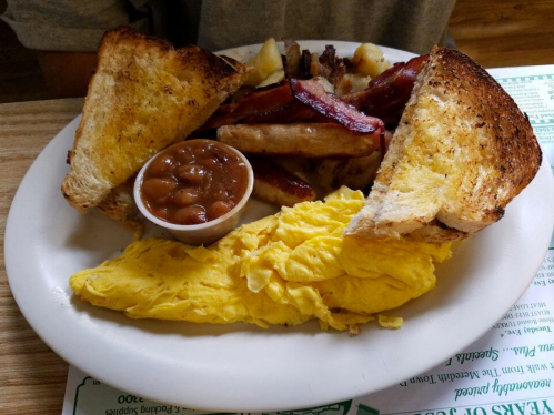 A plate of breakfast featuring toast, scrambled eggs, bacon, sausage, potatoes, and a side of baked beans.