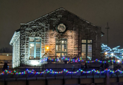 Historic building illuminated with colorful holiday lights at night, surrounded by festive decorations.
