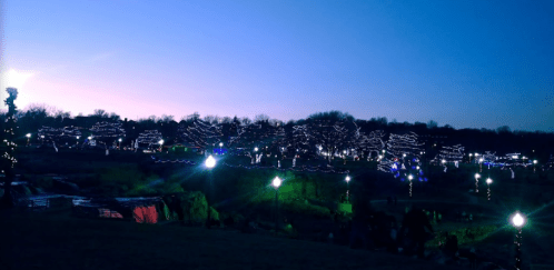A twilight scene of a park adorned with colorful lights on trees, creating a festive atmosphere.