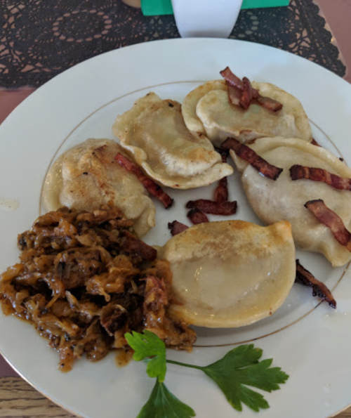 A plate of dumplings topped with bacon, served alongside sautéed cabbage and garnished with parsley.