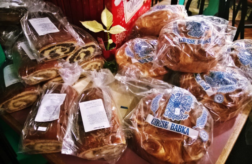 A display of wrapped cheese babka and other pastries on a table, with festive decorations in the background.