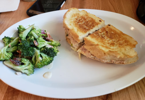 A toasted sandwich cut in half, served with a side of broccoli salad on a white plate.