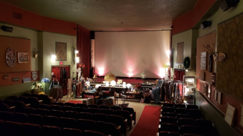 A vintage theater interior with red curtains, empty seats, and a stage set up for a performance or event.