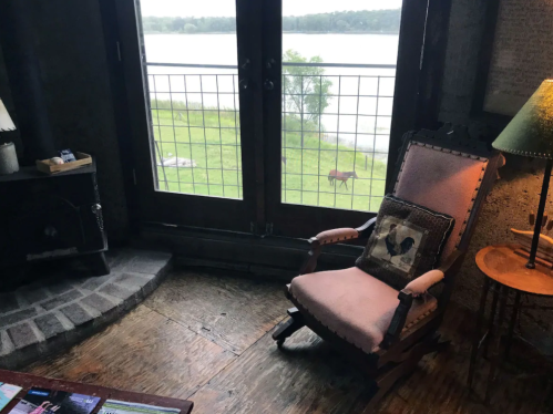 Cozy interior with a rocking chair, lamp, and view of a lake and grassy area through large glass doors.
