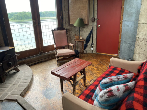 Cozy interior with a plaid sofa, wooden table, and vintage chairs, overlooking a scenic view through large windows.