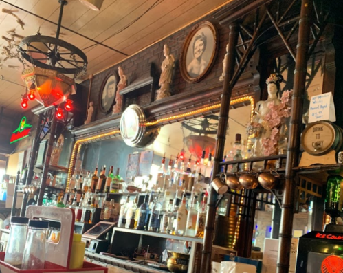 A vintage bar with ornate decor, mirrors, and shelves lined with various bottles of liquor. Red lights add ambiance.