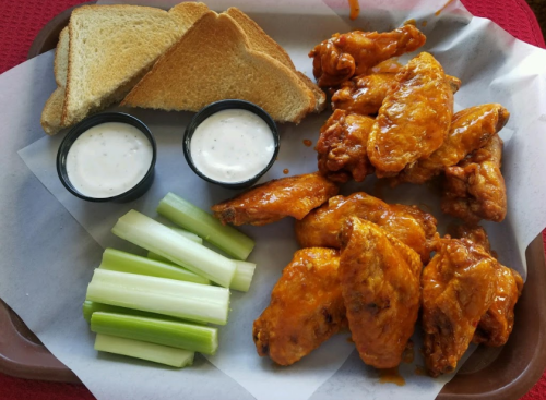 A tray with buffalo chicken wings, celery sticks, two cups of ranch dressing, and two slices of toasted bread.