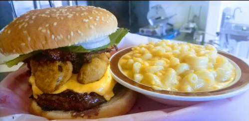 A sesame seed bun burger with cheese, lettuce, and fried pickles, served with a side of creamy macaroni and cheese.