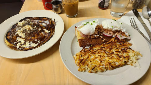 A plate with pancakes and scrambled eggs, alongside another plate with poached eggs on toast and hash browns.