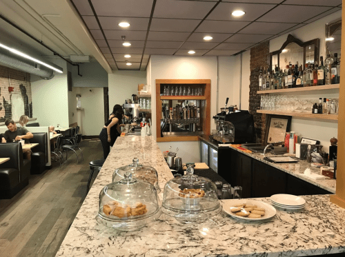 A cozy café interior featuring a marble counter, glass pastry displays, and a barista behind the coffee machine.