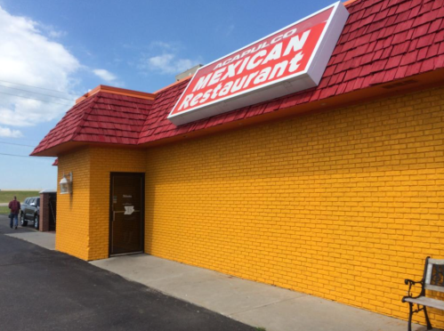 Bright yellow building with a red roof, featuring a sign that reads "Acapulco Mexican Restaurant." Clear blue sky above.