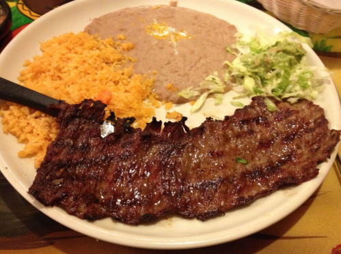 A plate featuring grilled steak, rice, refried beans, and shredded lettuce.