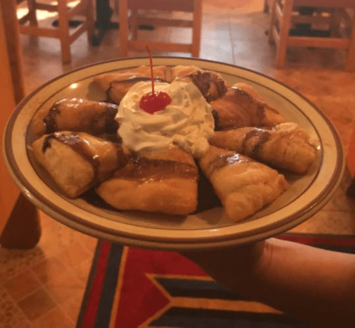 A plate of pastry triangles drizzled with chocolate sauce, topped with whipped cream and a cherry.