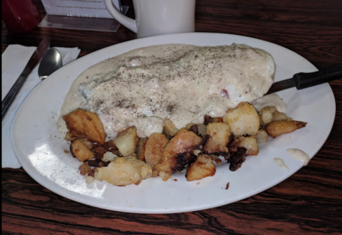 A plate of a large omelet covered in creamy gravy, served with crispy golden-brown potatoes on the side.