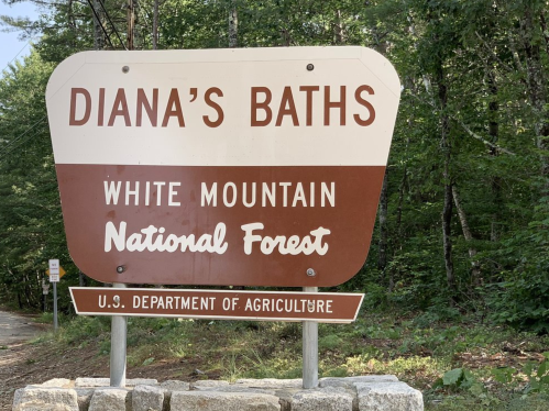 Sign for Diana's Baths in White Mountain National Forest, U.S. Department of Agriculture. Surrounded by trees.
