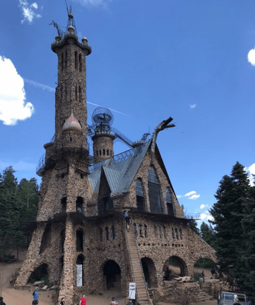 A unique stone castle with towers and intricate details, surrounded by trees and a blue sky.