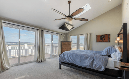 Bright bedroom with a beach view, featuring a large window, ceiling fan, and cozy bed.