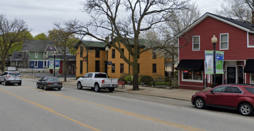 A street view featuring colorful buildings, parked cars, and trees in a small town setting.