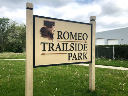 Sign for Romeo Trailside Park, featuring the park's name and a map outline, set against a grassy background.