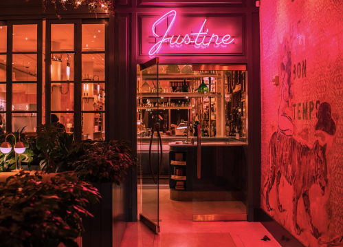 A vibrant restaurant entrance with a neon sign reading "Justine" and colorful decor, illuminated in warm tones.
