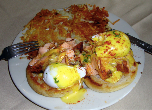 A plate of eggs Benedict with salmon on English muffins, topped with hollandaise sauce, served with crispy hash browns.
