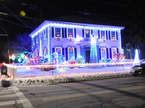 A brightly lit house decorated with colorful Christmas lights and festive ornaments, surrounded by snow.