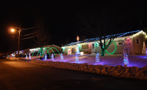 A festive house decorated with colorful Christmas lights, surrounded by snow, glowing in the night.