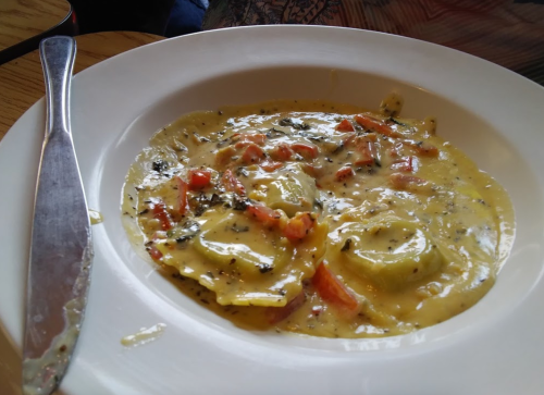 A plate of ravioli in a creamy sauce with diced tomatoes and herbs, accompanied by a knife on the side.