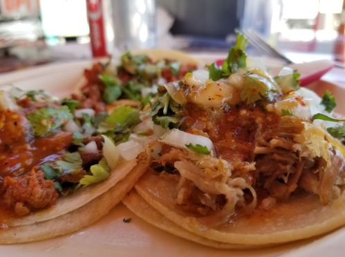Two tacos topped with cilantro, onions, and sauce, served on a plate with a side of meat.