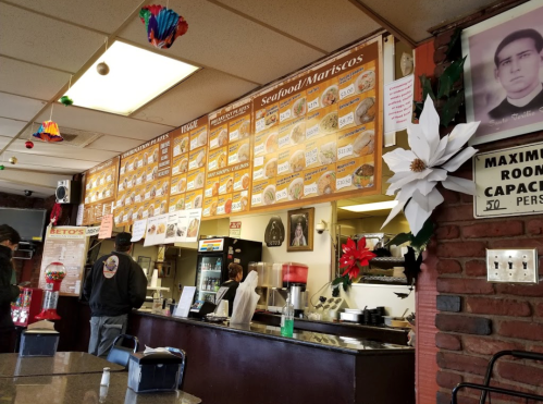 Interior of a seafood restaurant with a menu board, festive decorations, and customers at the counter.