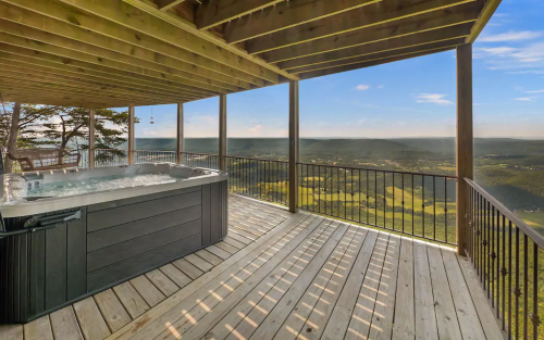 A hot tub on a wooden deck with a scenic view of rolling hills and a clear blue sky.