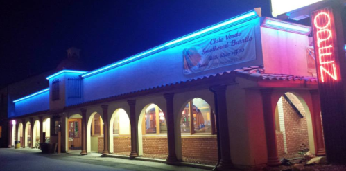 A brightly lit restaurant exterior at night, featuring blue neon lights and arched windows.