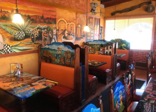 Colorful Mexican restaurant interior with vibrant murals and decorated booths. Warm, inviting atmosphere.