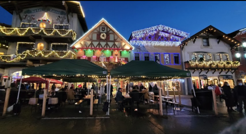Festive market scene with illuminated buildings and tents, bustling with people during twilight.