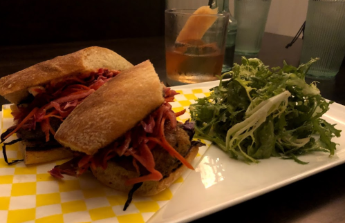 A plate with two sandwiches filled with shredded vegetables, accompanied by a side salad and a drink in a glass.