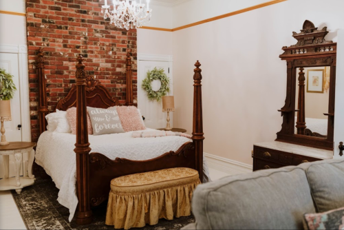Cozy bedroom featuring a vintage four-poster bed, brick accent wall, and elegant decor with a chandelier.