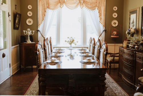 Elegant dining room with a long wooden table set for a meal, surrounded by chairs and adorned with decorative accents.
