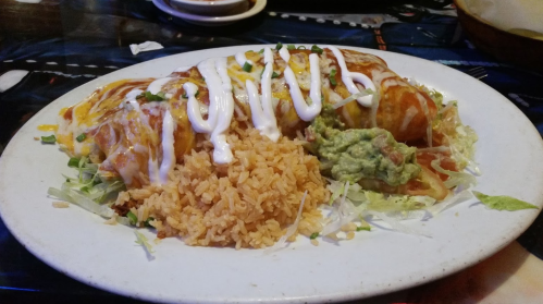 A plate of enchiladas topped with cheese and sour cream, served with rice, guacamole, and lettuce.