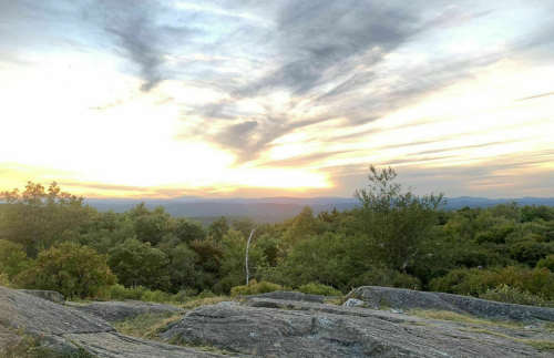 A scenic view of a sunset over a lush landscape, with rocky terrain and trees under a colorful sky.