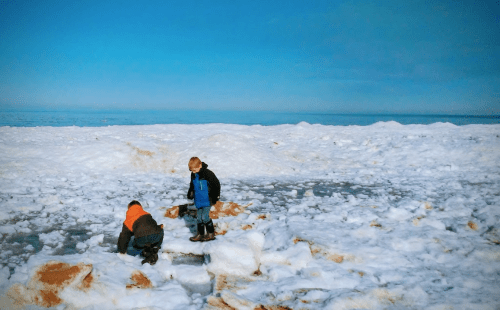 Two children play on a snowy landscape, exploring the icy terrain under a clear blue sky.