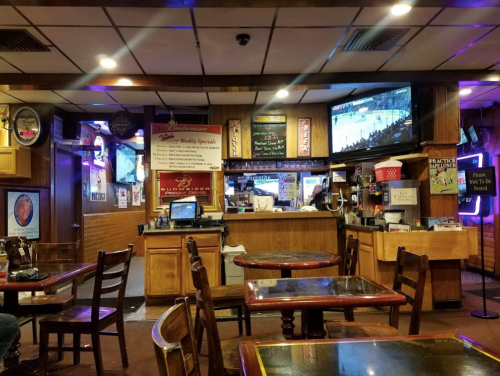 A cozy bar interior with wooden tables, a TV showing a sports game, and various signs on the walls.