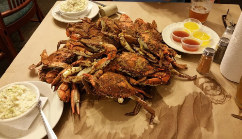 A large pile of seasoned crabs on a table, accompanied by dipping sauces and side dishes.