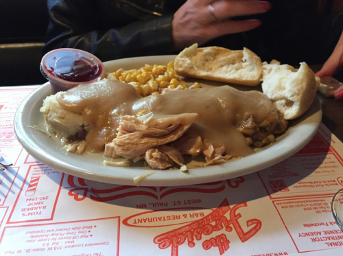 A plate of chicken and gravy over mashed potatoes, served with corn, a roll, and a side of cranberry sauce.