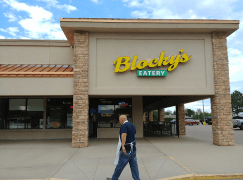 A person walks past the entrance of Blocky's Eatery, a casual dining restaurant with a stone facade.