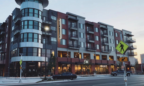 Modern multi-story building with retail on the ground floor and residential units above, set in an urban environment.