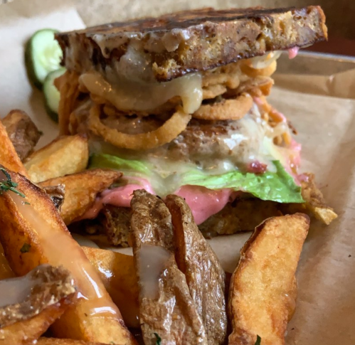 A hearty sandwich with lettuce, onion rings, and sauce, served with crispy potato wedges on the side.